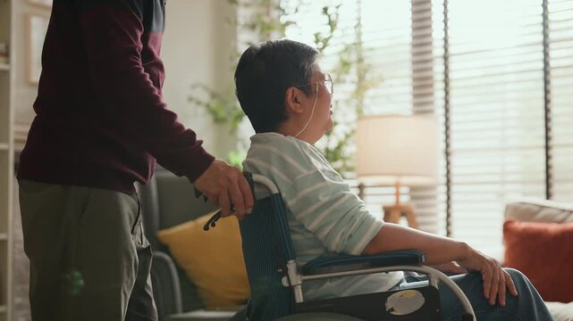 Asian senior couple at home, retired man in wheelchair embraced by loving woman, caregiving support, bonding and true love, warm living room lifestyle, family connection, compassion and lifelong partn