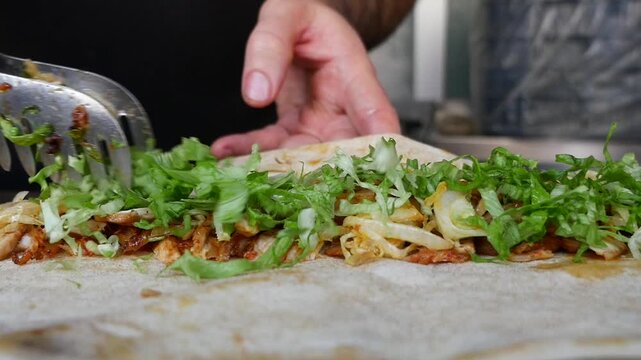 Someone prepares chicken wrap by putting lettuce and doner meat .