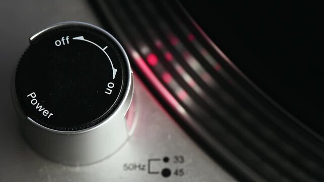 Close-up shot of a vintage turntable power knob being turned on, platter spins.