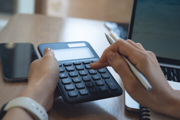 Doing finance, budgeting and tax calculation. Close up woman hand using calculator to calculate home finance, accounting with laptop computer on table, budget management, monthly expenses.