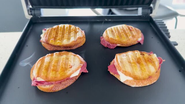 Four Pastrami and Cheese Panini Sandwiches Grilling on an Electric Press