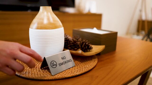 Hand Placing No Smoking Sign Next to Aromatherapy Diffuser on Table