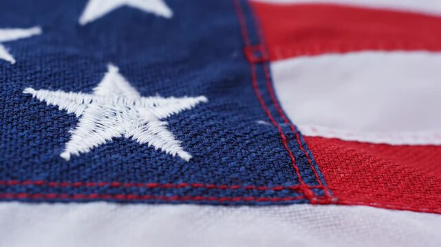 Extreme closeup texture of the American flag fabric, showing embroidered white stars on blue field and red and white stripes, patriotic symbol