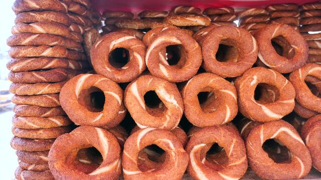 Freshly baked turkish simit bread with sesame seeds stacked in street food stall outdoors.