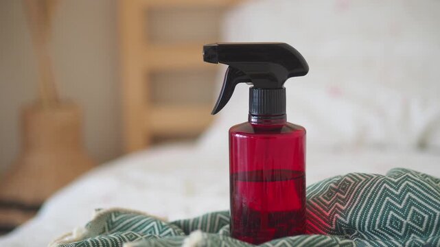 A red plastic spray bottle with a black trigger is on a green blanket in motion.