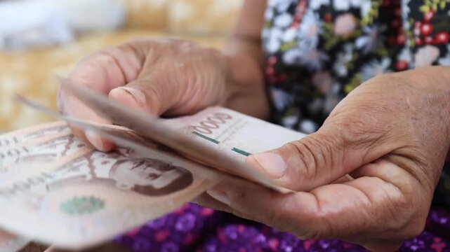 Elderly hands counting Thai banknotes Baht, Money close-up. Concept of retirement savings, pension income, financial security, budgeting, and senior financial planning