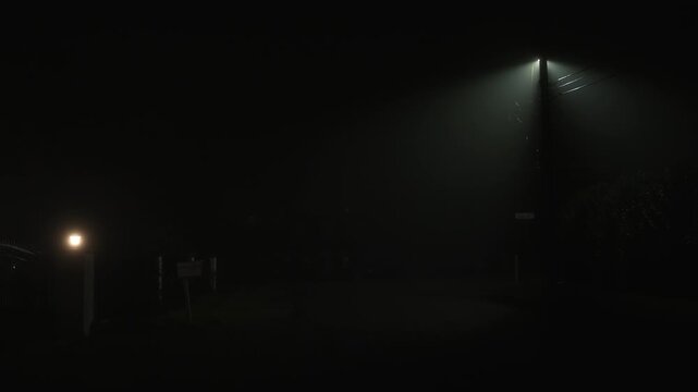 Foggy residential street at night with glowing street lamps creating moody cinematic atmosphere of quiet neighborhood with dense mist and low visibility