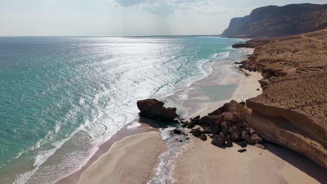 Aerial view of turquoise sea and sandy beach by desert cliffs. Sokotra, Yemen.