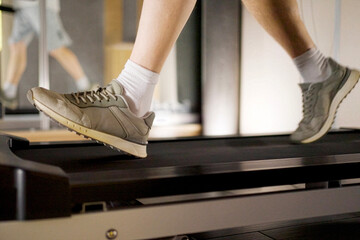 Close up of man's legs running on a treadmill in a gym. Low angle view of a person in sneakers...