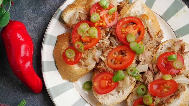 Gourmet tuna bruschetta with fresh tomatoes and green onions served on striped plate clip.
