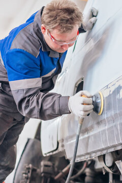 Technician in protective gear sanding the body of a car in an auto repair shop. Vehicle maintenance and repair service.