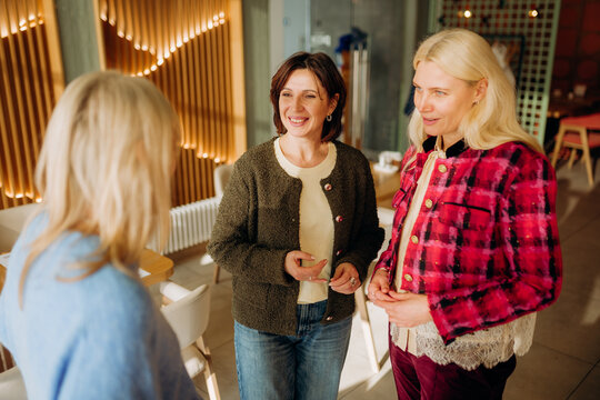 In a warm cafe setting, three women share joyful conversations, exchanging smiles and laughter over coffee. The cozy atmosphere enhances their cheerful exchange during a sunny afternoon.