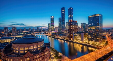 Obraz premium Twilight skyline of a modern city with illuminated riverfront buildings and skyscrapers