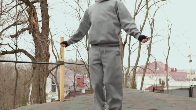 Medium shot focusing on legs of a man in grey sweatpants jumping rope. Sportsman performing intense skipping rope routine at an outdoor fitness area