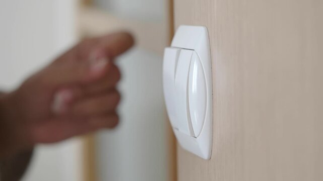 Woman finger pressing light switch button on wall in room close up turning lights on off.