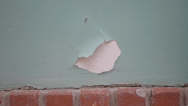 Peeling paint reveals old plaster texture on exterior wall near brickwork.