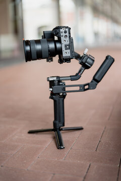 Mirrorless camera with zoom lens mounted on motorized gimbal tripod on pavement, showing portable filmmaking equipment for creator business and video production