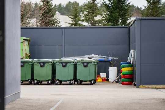 Waste collection bins lined up in service yard near industrial fence, showing urban sanitation logistics, recycling operations, and facility management