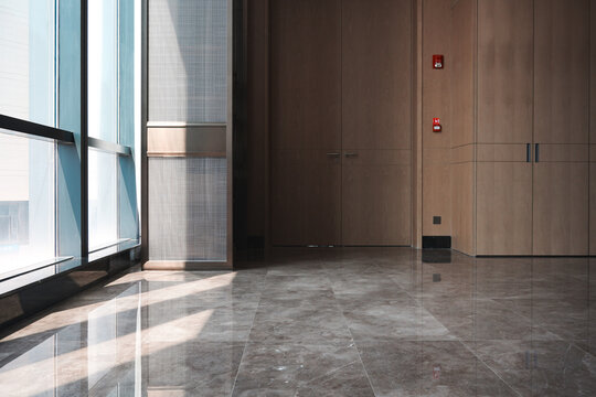 Modern office interior featuring wooden doors walls and floor-to-ceiling windows with marble flooring and natural light reflection