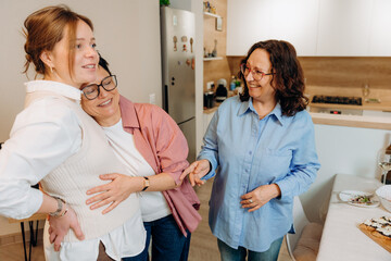 Obraz premium Three women enjoy a heartfelt moment together in a cozy kitchen. Laughter fills the air as they share stories and celebrate friendship, surrounded by delicious food and warm smiles.