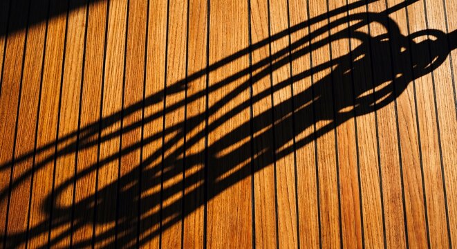 Geometric shadows of a railing cast on premium teak wood decking under bright sunlight creating a minimal abstract pattern
