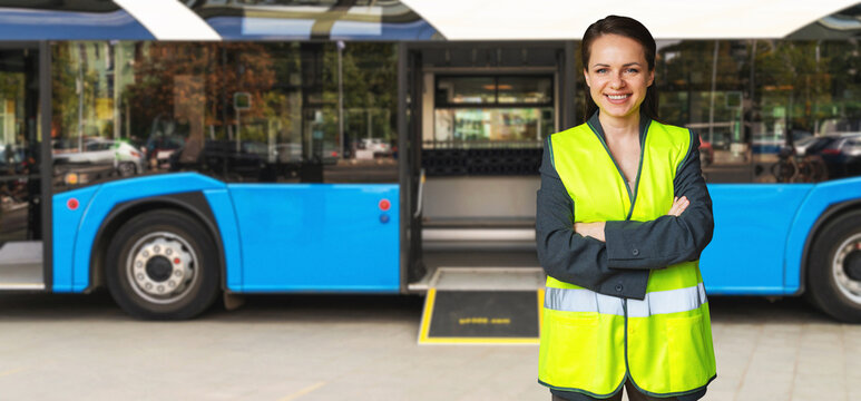 Smiling female bus driver wearing high vis vest standing in front of bus.