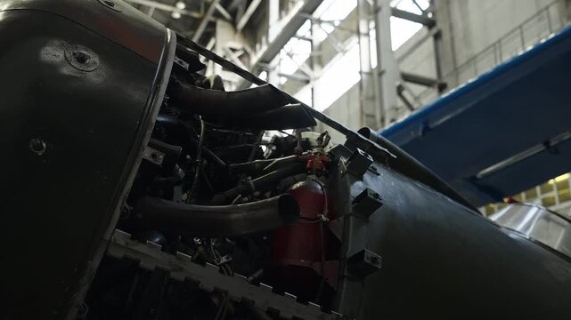 Close-up view of a propeller aircraft undergoing maintenance inside an industrial hangar, exposing engine components, landing gear, and fuselage details under workshop lighting