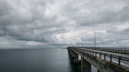 Fototapeta premium Long empty bridge stretching into distance under dramatic cloudy sky of journey direction and future path concept