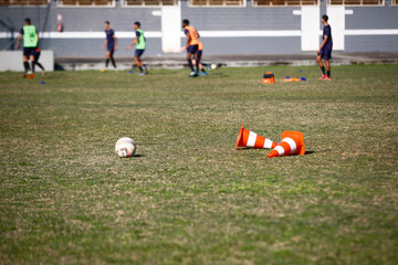 Obraz premium Training football equipments in a green grass football field while athletes practice during a sunny day 
