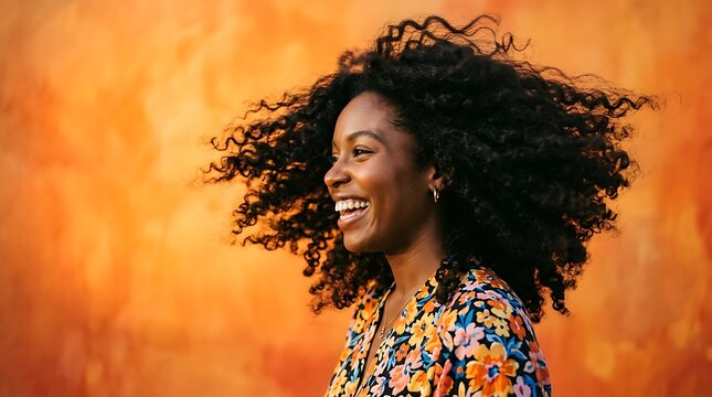 Joyful Black Woman with Voluminous Curly Hair Smiling Against Orange Wall.