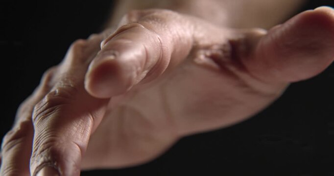 Intimate close-up of a human hand reaching out from the darkness, symbolizing a gesture of assistance, a plea for help, or an offer of connection and support