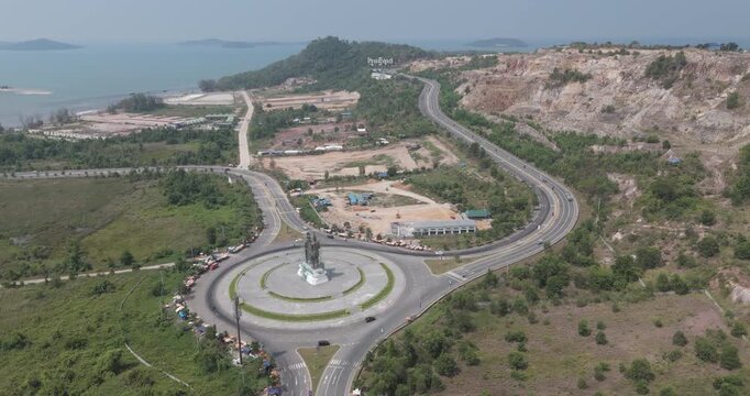 aerial view of the Preah Thong Neang Neang statue at a roundabout near Bay of Lights in Sihanoukville,, featuring a winding coastal highway and a rocky quarry.