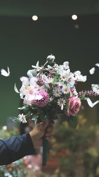 화사한 꽃다발 주위로 팔랑거리며 모여드는 하얀 나비 떼와 사람의 손 (A group of white butterflies fluttering and gathering around a beautiful flower bouquet held by a person)