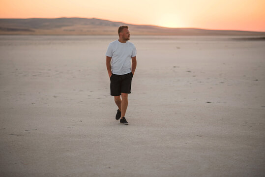 Man walking alone in a vast, dry landscape during a beautiful sunset