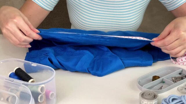 A girl measures a torn hole in her blue shorts with a measuring tape. Conceptual imagery of damaged clothing, fabric repair, and the sewing process.