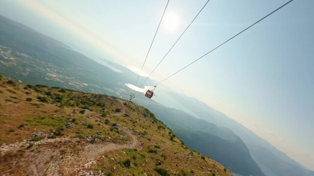 Cinematic FPV drone footage flying past a red cable car cabin with a breathtaking panoramic view of the Bay of Kotor and Lovcen National Park during summer.