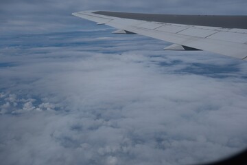 Obraz premium Airplane wing soaring above fluffy clouds in blue sky.
