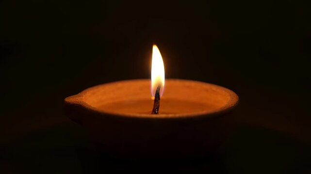 Closeup of a glowing oil lamp candle flame in darkness, creating a calm and spiritual atmosphere. Ideal for meditation, prayer, Diwali, and peaceful mood visuals.
