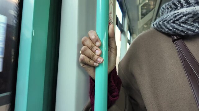 Person holding pole on public transport, close up on hand and scarf, moving through city.
