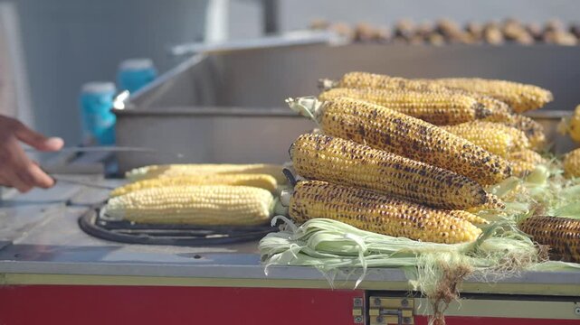 Street vendor cooking corn on grill for customers at outdoor market stall footage.