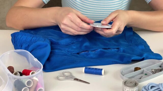 A girl prepares to mend shorts and takes needles from a sewing kit, preparing the tools for clothing repair. Concepts of home sewing, handicrafts, and DIY repairs.