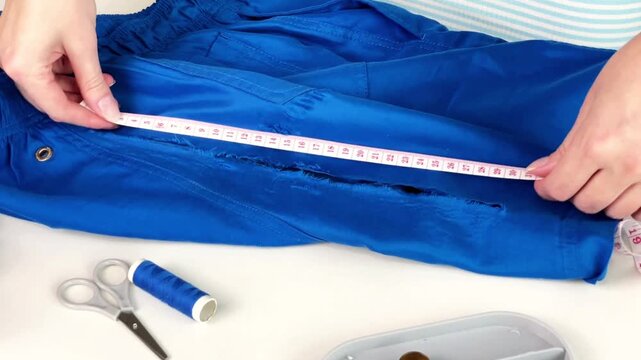 A woman examines a hole in her shorts and measures its size with a tape measure. Concept of clothing repair, sewing, and textile damage assessment.