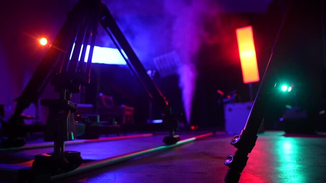 Close view of a camera slider on studio floor with colorful lights, smoke, and backstage equipment. Concept of video production, filming technology, concert setup, media, and creative industry.