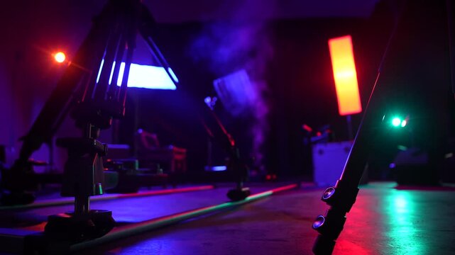 Close view of a camera slider on studio floor with colorful lights, smoke, and backstage equipment. Concept of video production, filming technology, concert setup, media, and creative industry.