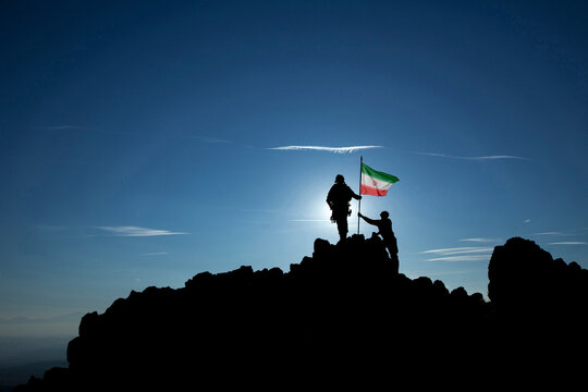 Silhouettes of anonymous soldiers raising Iran flag on mountain peak, teamwork, victory, war concept, copy space.