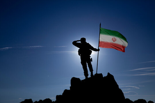 Silhouette of an unrecognizable soldier saluting with Iran flag on mountain peak, dramatic sky, war concept, copy space.