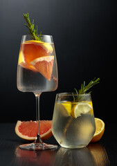Gin tonic with ice, rosemary, lemon, and grapefruit on a black wooden table.