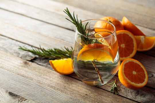 Gin tonic with ice, rosemary,  and orange slices on an old wooden table.