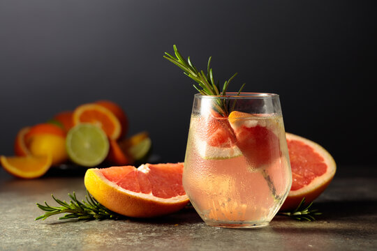 Cocktail gin tonic with ice, rosemary, and grapefruit on a stone table.