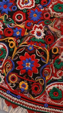 Close-up of a traditional black manton shawl featuring vibrant and intricate folk embroidery with colorful floral patterns, paisley motifs, and textile fringe details.